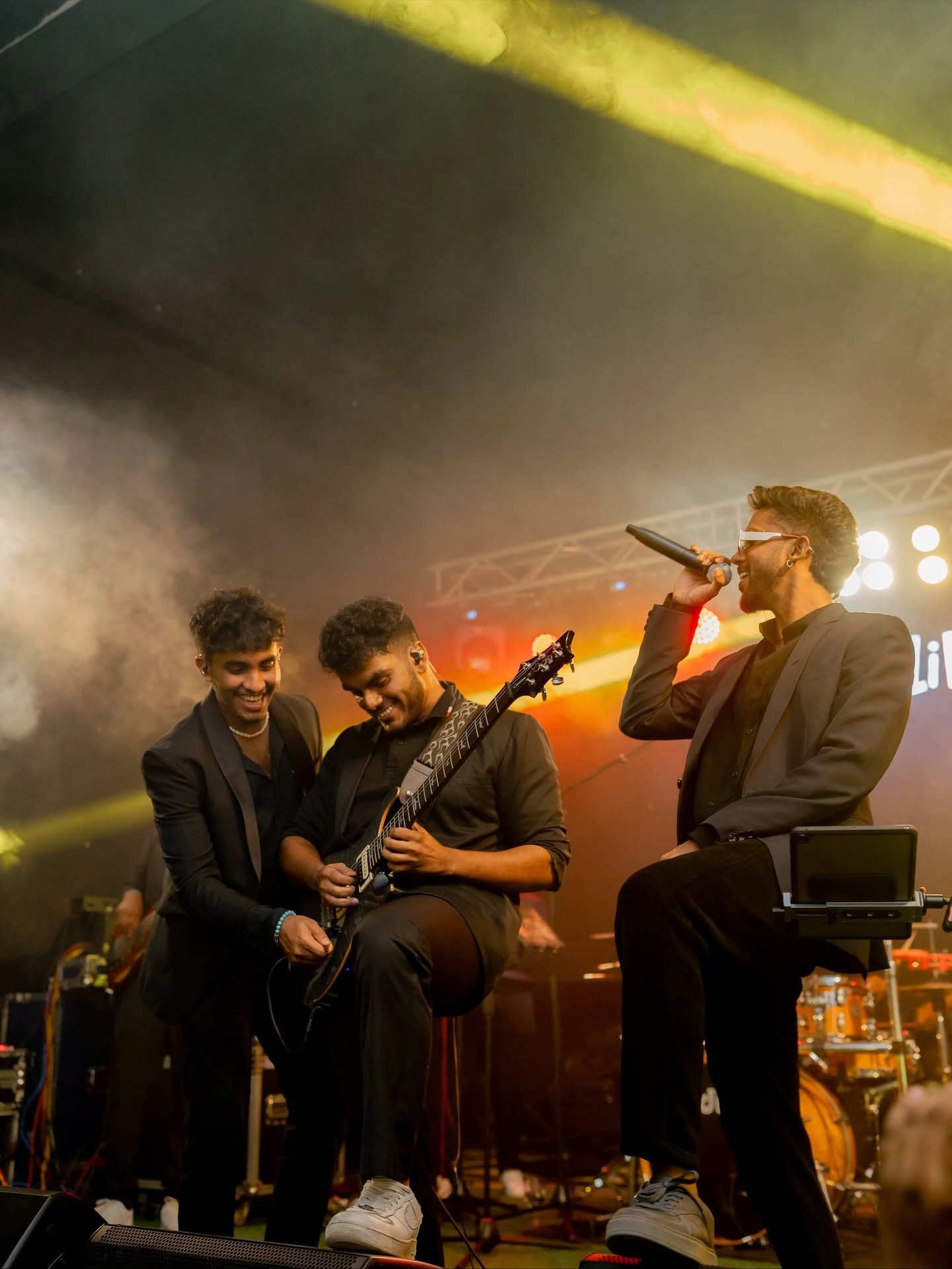 Three band members laughing as one plays guitar